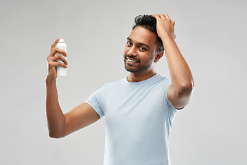 Image showing smiling indian man applying hair spray over gray