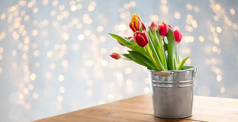 Image showing red tulip flowers in bucket on table over lights