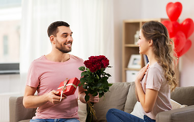 Image showing happy man giving woman flowers and present at home