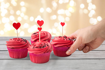 Image showing close up of hand taking cupcakes with heart sticks