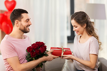 Image showing happy man giving woman flowers and present at home