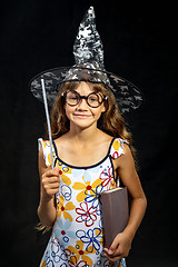 Image showing Girl sorceress, with a book and a magic wand, in a hat, on a black background