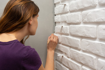 Image showing A house painter tends to paint a gray corner of the wall with a small tassel