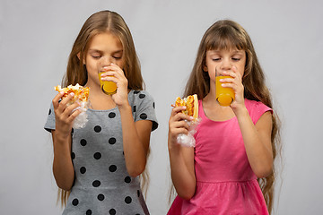 Image showing Two girls drink juice and eat a bun