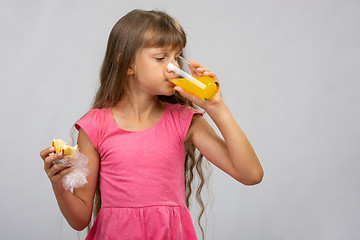 Image showing A girl drinks orange juice and eats a bun