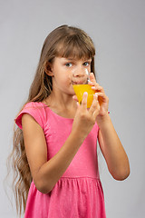 Image showing The girl drinks orange juice from a glass and looks at the frame