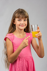 Image showing A girl holds a glass of orange juice in her hand and points her finger at it