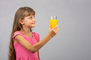 Image showing A girl holds a glass of juice in her hand and looks at the empty space on the right