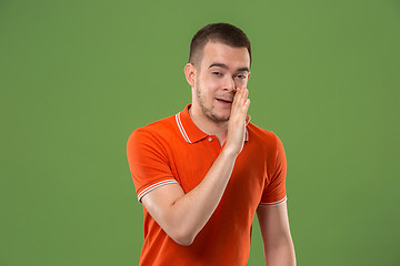 Image showing The young man whispering a secret behind her hand over green background