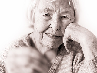 Image showing Sad elderly woman sitting at the table at home and looking miserably at only remaining coin from pension in her hand.