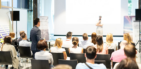 Image showing Businessman in audience standing and asking question to speeker at business conference.