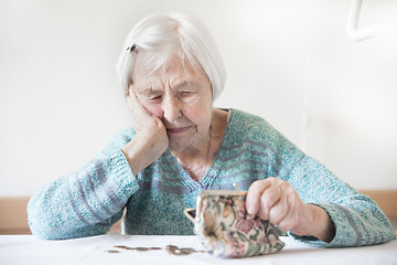 Image showing Concerned elderly woman sitting at the table counting money in her wallet.