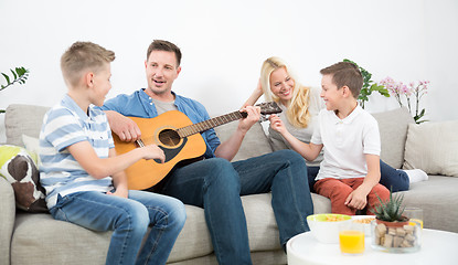 Image showing Happy caucasian family smiling, playing guitar and singing songs together at cosy modern home