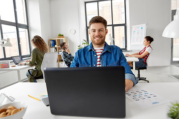 Image showing smiling creative man with laptop working at office
