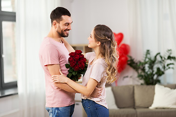 Image showing happy couple with bunch of flowers hugging at home