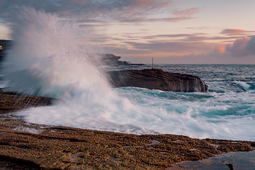 Image showing Waves splash high onto the coastal rock shelf at sunrise