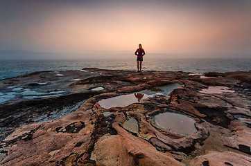 Image showing Woman standing on sandstone rocks with foggy coastal sunrise