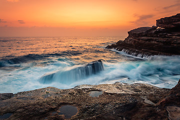 Image showing Stunning sunrise and waves crash over rocks on the Sydney sea coast