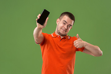 Image showing The happy man showing at empty screen of mobile phone against green background.