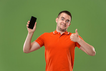 Image showing The happy man showing at empty screen of mobile phone against green background.