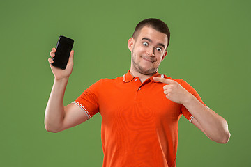 Image showing The happy man showing at empty screen of mobile phone against green background.