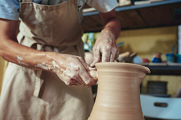 Image showing Creating a jar or vase of white clay close-up. Master crock. Man hands making clay jug macro.