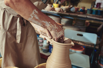 Image showing Creating a jar or vase of white clay close-up. Master crock. Man hands making clay jug macro.