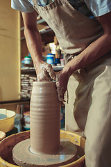 Image showing Creating a jar or vase of white clay close-up. Master crock. Man hands making clay jug macro.