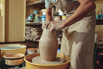 Image showing Creating a jar or vase of white clay close-up. Master crock. Man hands making clay jug macro.
