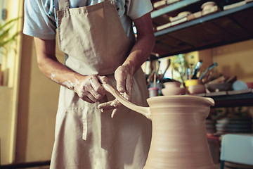 Image showing Creating a jar or vase of white clay close-up. Master crock. Man hands making clay jug macro.