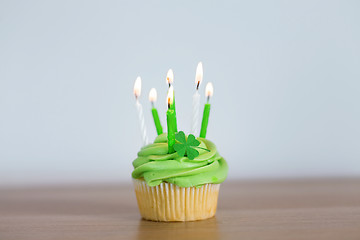 Image showing green cupcake with six burning candles on table