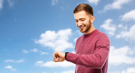 Image showing smiling young man checking time on wristwatch