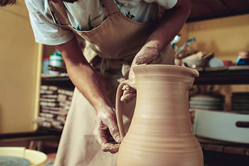 Image showing Creating a jar or vase of white clay close-up. Master crock. Man hands making clay jug macro.