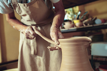 Image showing Creating a jar or vase of white clay close-up. Master crock. Man hands making clay jug macro.