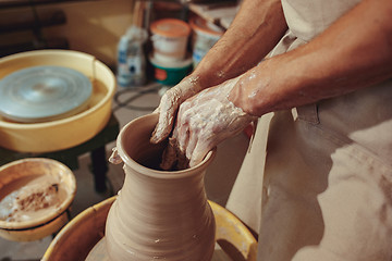 Image showing Creating a jar or vase of white clay close-up. Master crock. Man hands making clay jug macro.