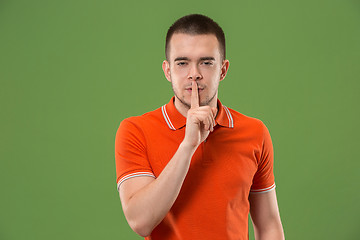 Image showing The young man whispering a secret behind her hand over green background