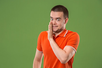 Image showing The young man whispering a secret behind her hand over green background