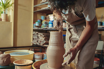 Image showing Creating a jar or vase of white clay close-up. Master crock. Man hands making clay jug macro.