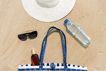 Image showing beach bag, sunscreen, sunglasses and hat on sand