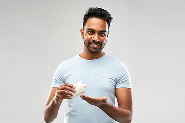 Image showing happy indian man applying lotion to his hand