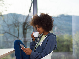 Image showing black woman drinking coffee and using a mobile phone  at home