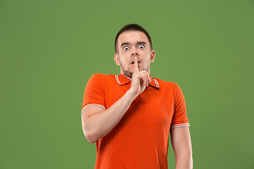 Image showing The young man whispering a secret behind her hand over green background