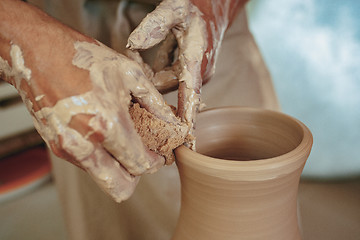 Image showing Creating a jar or vase of white clay close-up. Master crock. Man hands making clay jug macro.