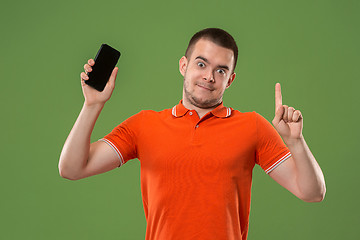 Image showing The happy man showing at empty screen of mobile phone against green background.