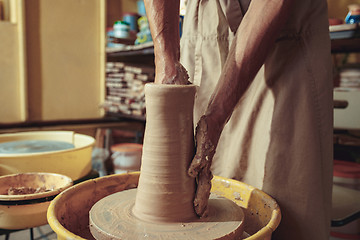 Image showing Creating a jar or vase of white clay close-up. Master crock. Man hands making clay jug macro.