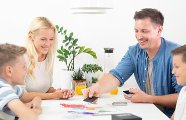 Image showing Happy young family playing card game at dining table at bright modern home.