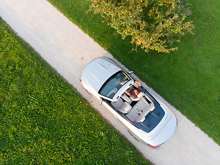 Image showing Aerial view of successful man driving and enjoying his silver convertible luxury sports car on the open country side road
