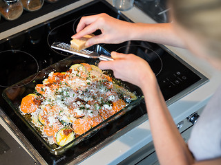 Image showing Female chef grinding parmesan cheese on row vegetarian dish ingredients in glass baking try before placing it into oven. Healthy home-cooked everyday vegetarian food