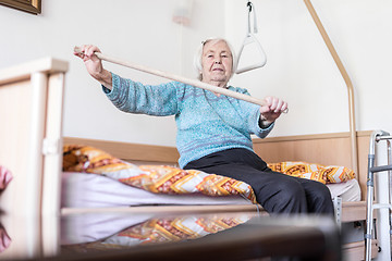 Image showing Elderly 96 years old woman exercising with a stick sitting on her bad.