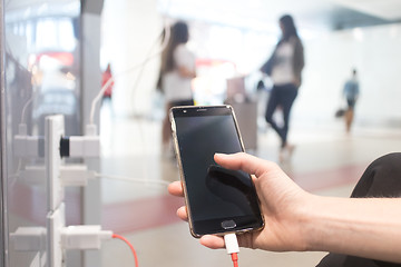 Image showing Female hands holding and using smartphone while charging it in a public place using electric plug and a charging cable